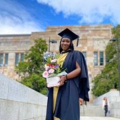 Consulata Bilal stands in a graduate robe with some flowers.